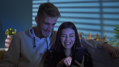 pareja feliz riendo mirando la pantalla del teléfono inteligente por la noche en casa.