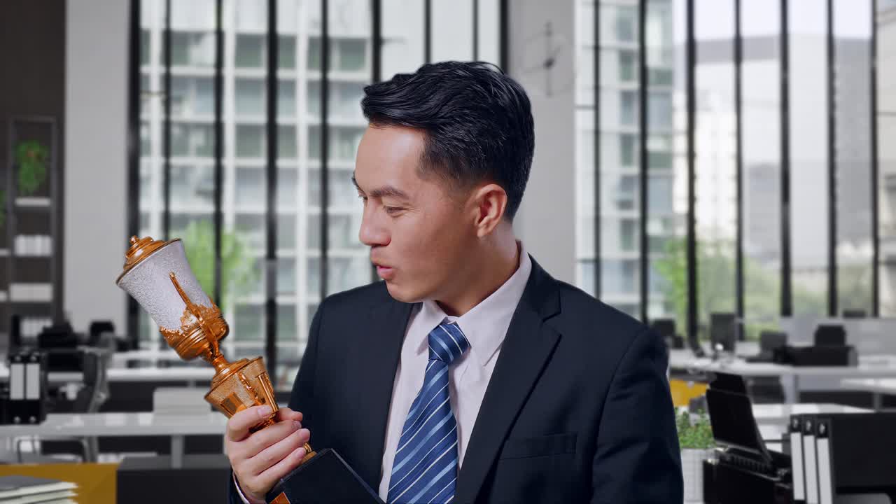 Close Up Of Asian Business Man In A Suit And Tie With A Gold Medal Looking At A Gold Trophy In His Hands And Saying Wow Being Happy Winning As The First Winner In Office
