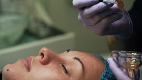 Cosmetologist covers the face of Caucasian woman with lotion. Beautician uses wide brush in work. Extreme close up.