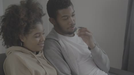 joven pareja afroamericana divirtiéndose mientras ve una película en la televisión. le da a su novia palomitas de maíz para comer