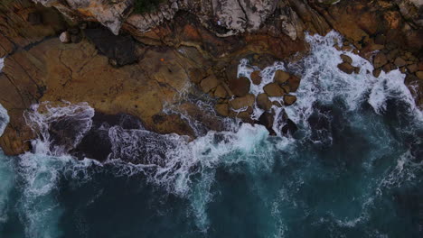 top view of blue green ocean waves smashing against rocky coastline in australia