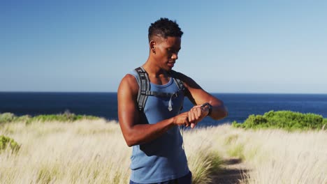 homme afro-américain qui court à travers le pays en utilisant une montre intelligente dans la campagne près de la côte