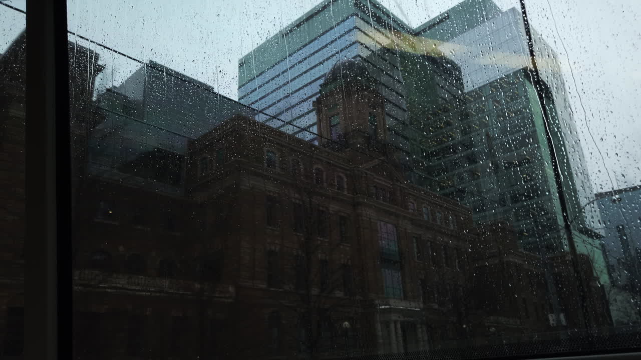 punto de vista del pasajero que viaja mirando por la parte trasera de un tranvía a través de una ventana empapada de lluvia en los edificios de la ciudad que pasan