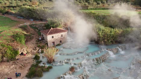 Hermosa-Fuente-Termal-Geotérmica-Con-Vapor-Que-Se-Eleva-Junto-Al-Antiguo-Edificio-En-Italia,-Saturnia