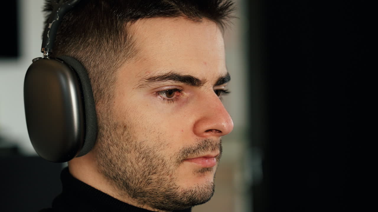 Close-up of a young man wearing headphones, deeply focused while working or studying at home. Cozy environment with soft natural light and modern freelance vibe