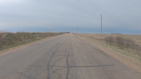 Rear-window-view-while-driving-on-an-old-asphalt-road-between-harvested-fields-in-rural-south-central-Nebraska-on-a-cloudy-winter-day