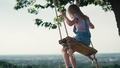 rear view blonde girl swinging high in summer day.