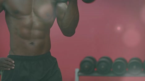 Spots-of-light-against-mid-section-of-african-american-fit-man-working-out-with-dumbbells-at-the-gym