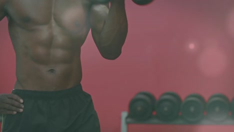 puntos de luz contra la sección media del hombre en forma afroamericano que hace ejercicio con pesas en el gimnasio