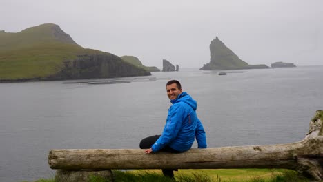 hombre guapo contempla las islas feroe mirando a drangarnir y tindholmur y sonriendo a la cámara
