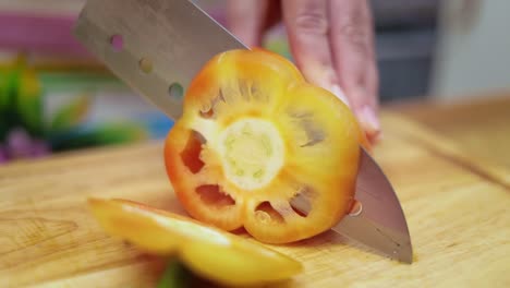 female hands of housewife with a knife cut fresh bell pepper on chopping board kitchen table