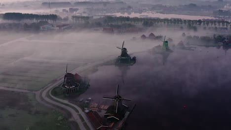 dron lata nad młynami wiatrowymi zaanse schans z dużą mgłą podczas wschodu słońca w holandii.