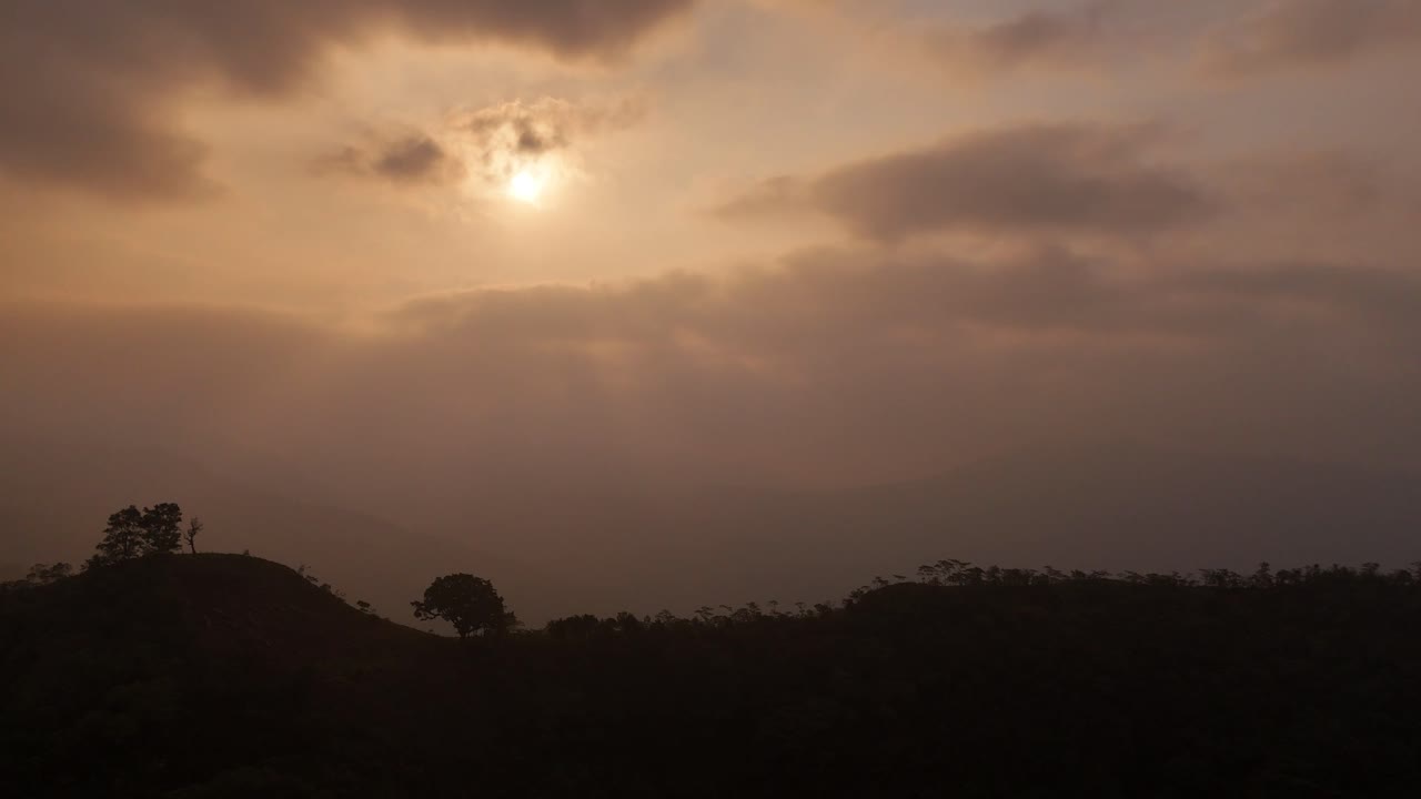 The sun hides behind clouds, casting an orange glow through the hidden sunlight in the sky.
