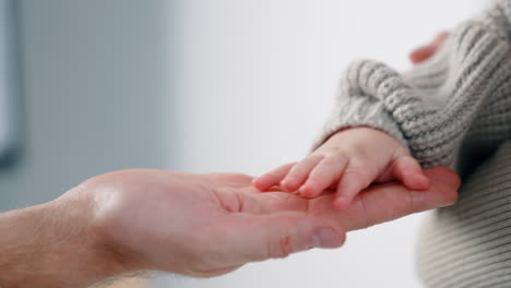 hand of a little unrecognized baby wearing a grey sweater. infant's hand is on the male adult hand. close up. white backdrop.