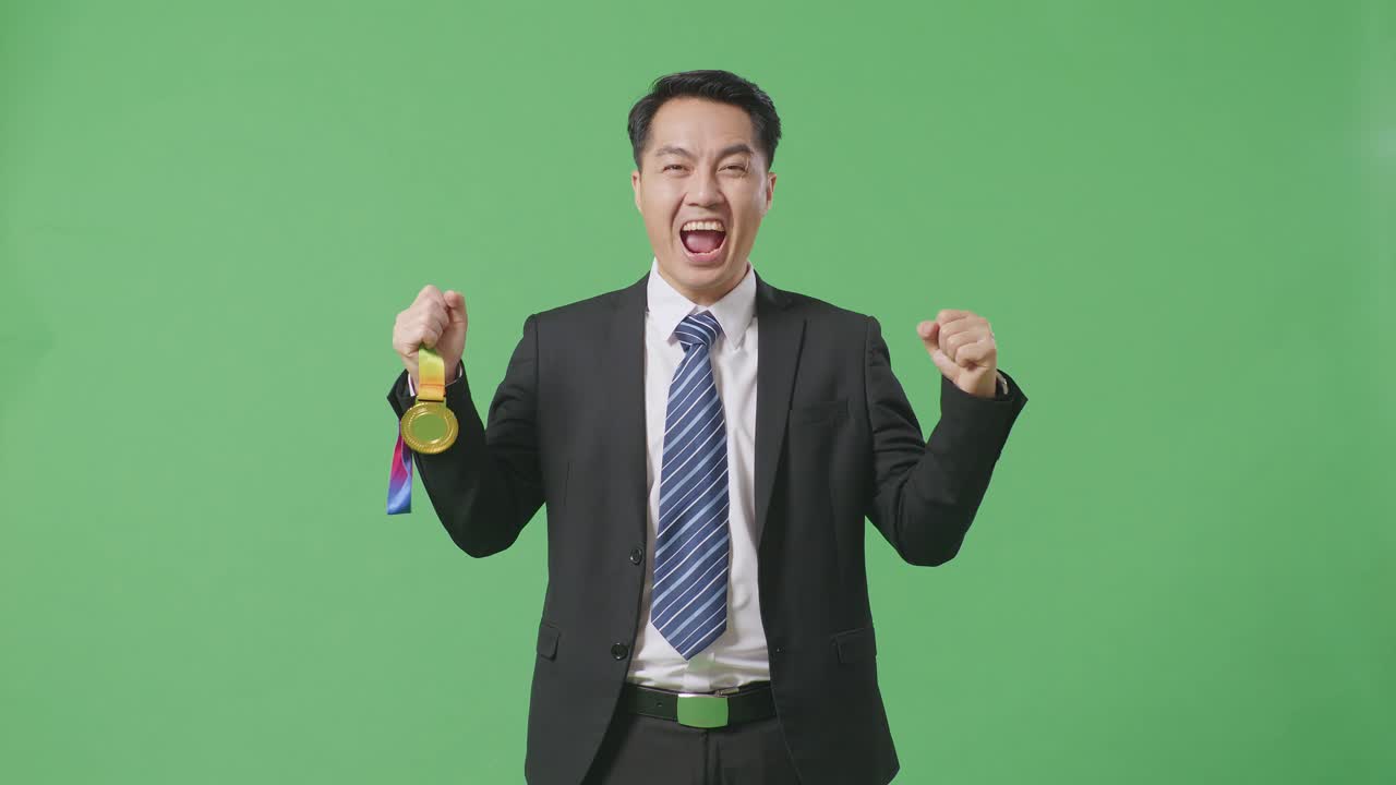 슈트와 타이를 입은 아시아 사업가, 금메달을 바라보며 울부는 골, 스튜디오의 녹색 스크린 배경에서 첫 번째 우승자로 우승을 축하하는