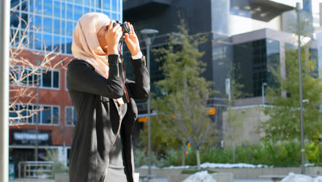vista frontal de una joven asiática en hijab haciendo clic en fotos con cámara digital en la ciudad 4k