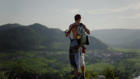 man puts on shirt, sun flare, looking over sky green mountain landscape in the background, peaceful sunlight tourist sunny, male person enjoying the view