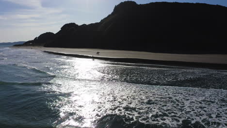 New-Zealand-horseback-riding-on-the-beach-of-Raglan,-couple-rides-together-observing-the-coastline