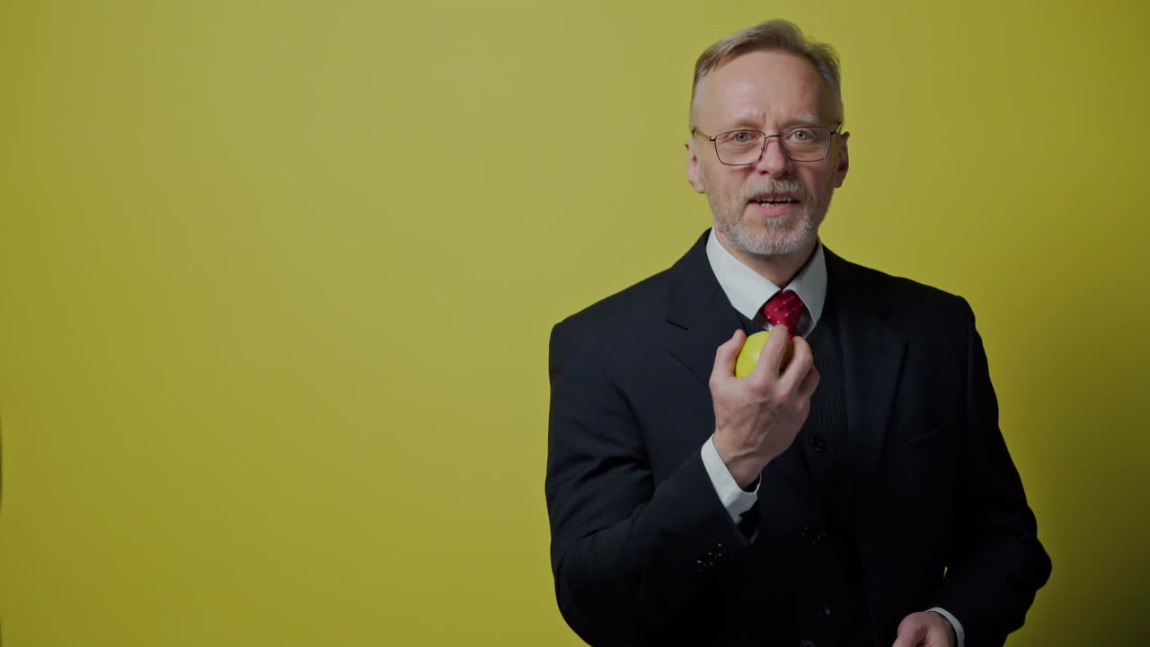 Portrait of happy mature man with apple. Smiling old businessman in costume playing with green apple on the yellow background.