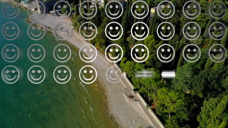 digital composition of rows of multiple smiling face emojis against aerial view of the beach