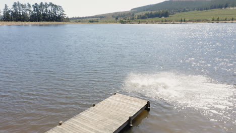 Vista-Aérea-Amigos-Felices-Saltando-Del-Embarcadero-En-El-Lago-Divirtiéndose-Chapoteando-En-El-Agua-Disfrutando-De-La-Libertad-En-Las-Vacaciones-De-Verano-Drone-Aéreo