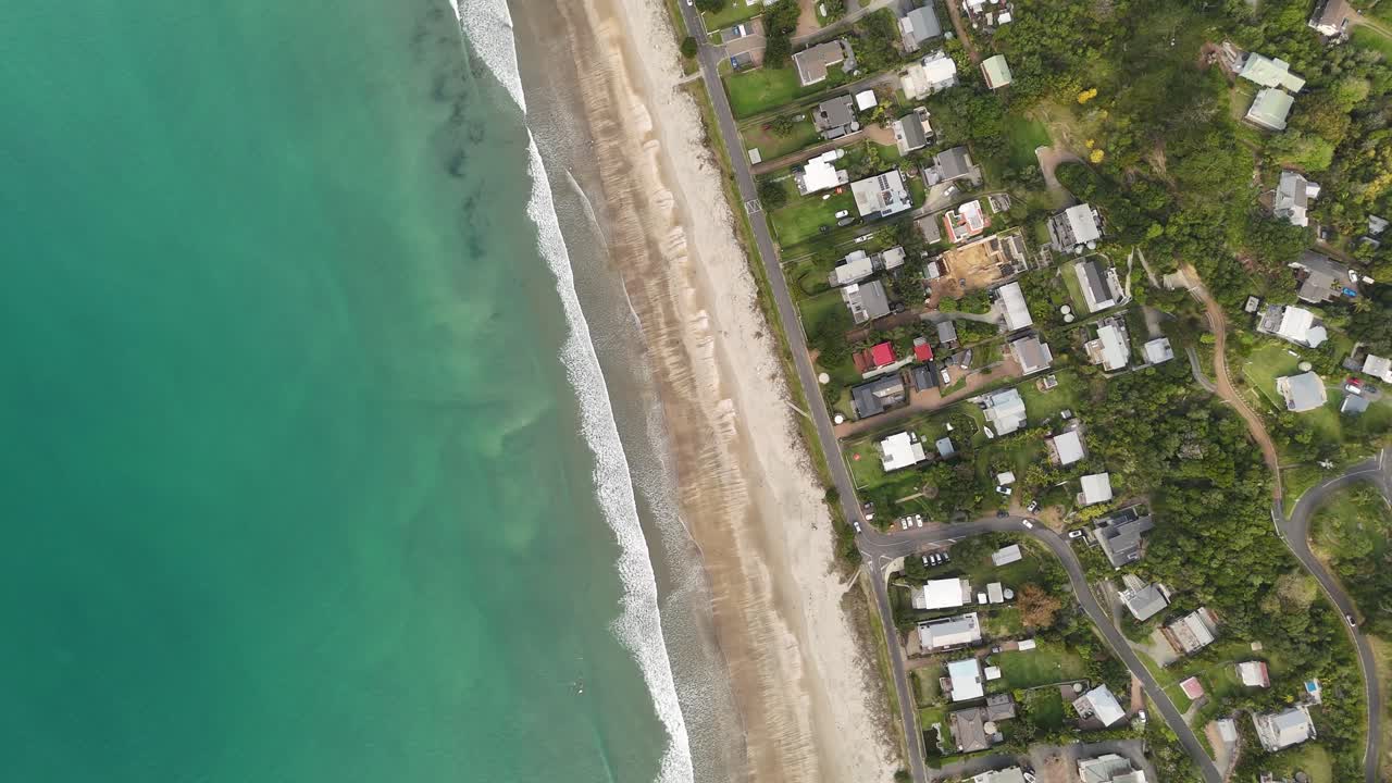 Onetangi Beach, Waiheke Island, turquoise waves, sandy shore, and coastal village, New Zealand. Aerial top-down view