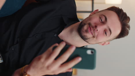 joven barbudo haciendo una llamada de teléfono inteligente conversación en línea con amigos sentados en el sofá en casa