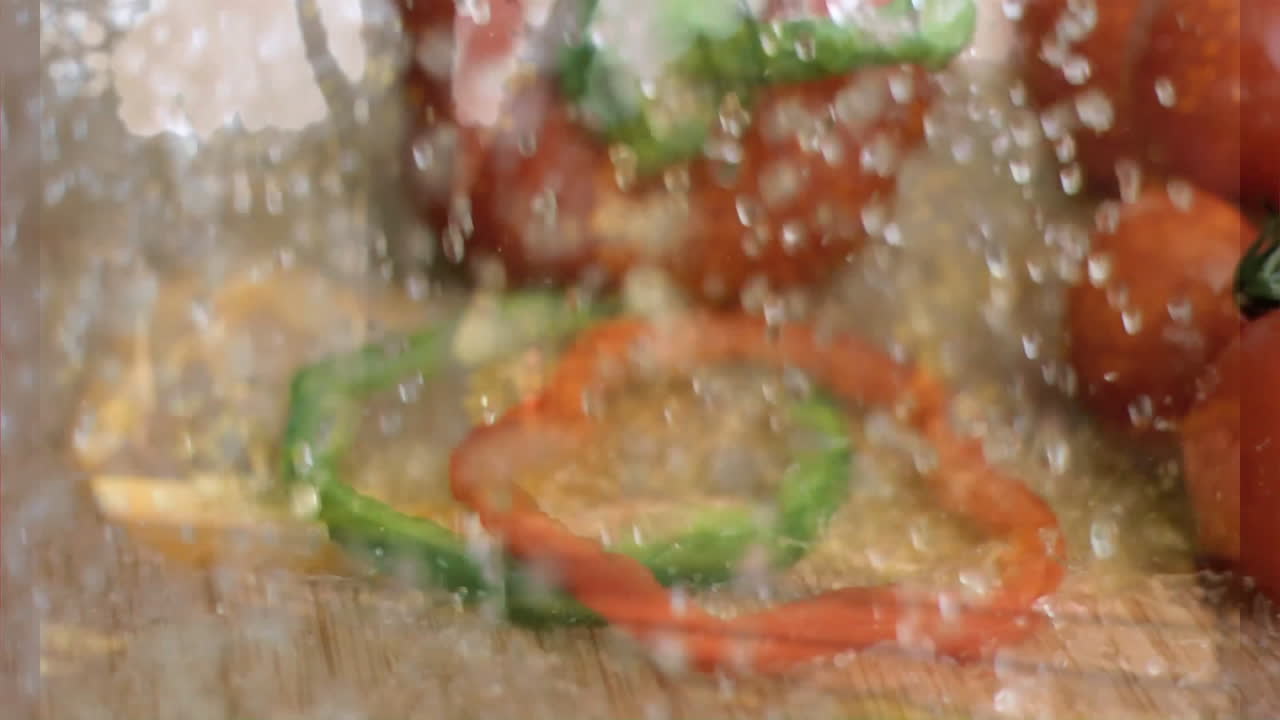 Sliced red and green bell peppers with water splashes on wooden surface