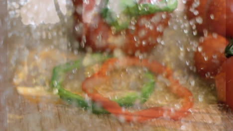 sliced red and green bell peppers with water splashes on wooden surface