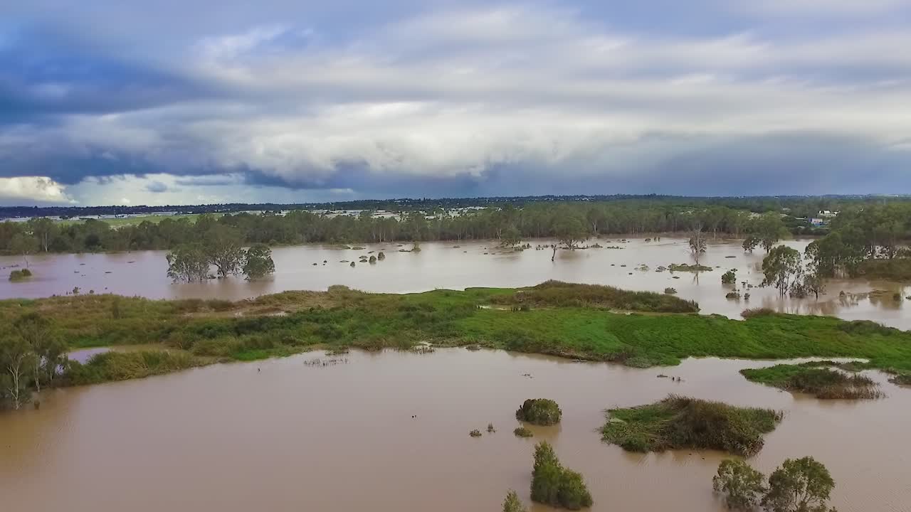 Queensland, NSW, Australia, February floods - moving backwards over inundated bushland and dirty brown floodwaters in suburban Brisbane, under stormy and threatening skies