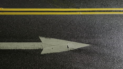 segni di freccia bianca sulla strada asfaltata con auto che guidano in città di notte