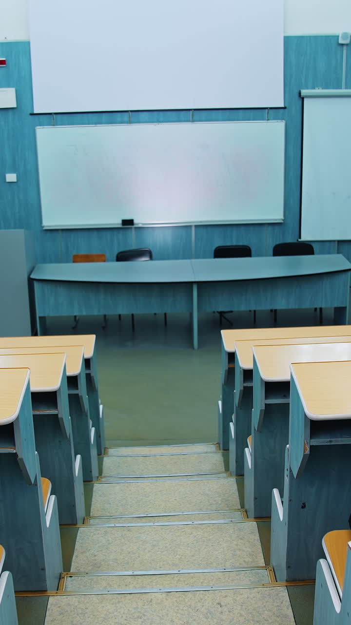 Empty auditorium. Modern lecture hall in the university. Wooden desks in front of blackboard and multimedia board in conference hall. Vertical video