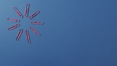 Red-paper-clips-are-arranged-in-a-circular-pattern-on-a-blue-background,-with-copy-space