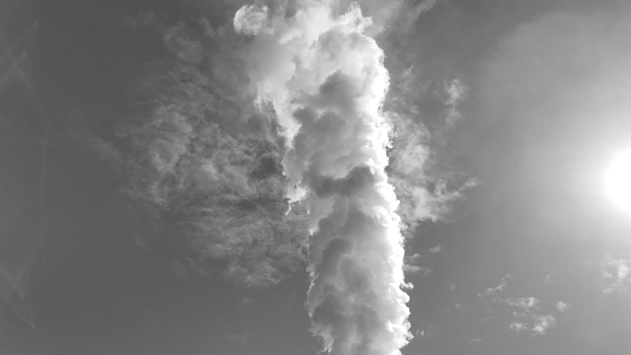 Thick smoke rises from a chimney, contrasting with the bright sun in a clear sky, highlighting environmental concerns