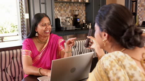 smiling indian woman in traditional sari using laptop and pointing at smartphone