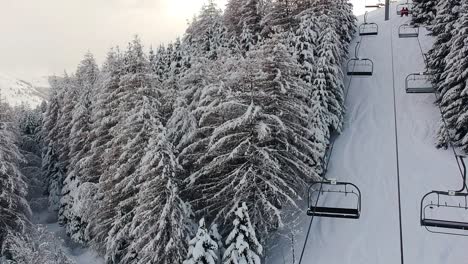 drone-aerial-circular-view-of-ski-lift-passing-in-between-tall-snow-covered-trees-in-the-french-alpes