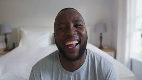 Portrait-of-african-american-man-smiling-while-sitting-on-the-bed-at-home