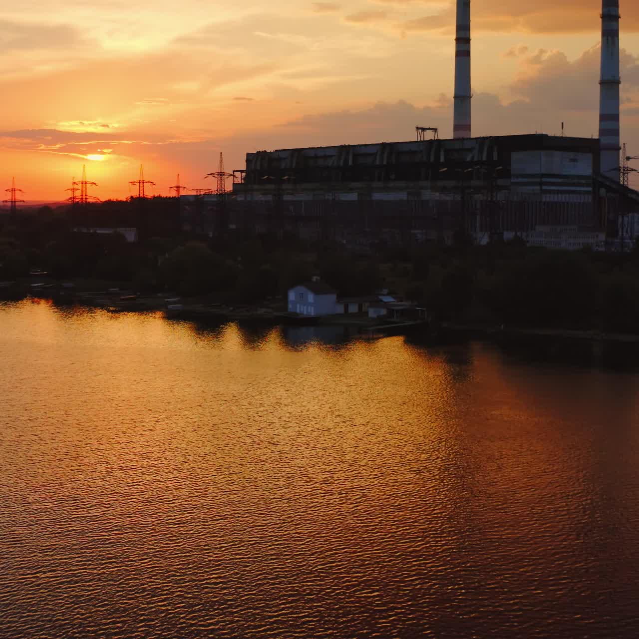 Harmful industry near the water in the evening. Dark silhouette of industrial zone near the river at sunset. Manufacturing in nature. View from the air.