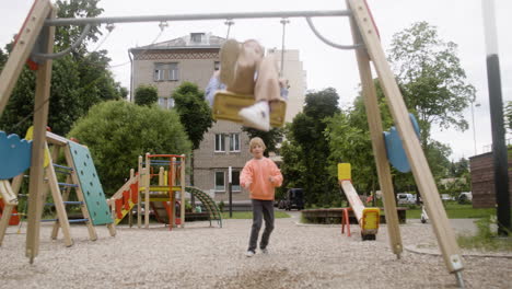 front view of little girl with down syndrome wearing hoodie swinging on a swing in the park on a windy day. her male friend pushing her while her female friend take a photo