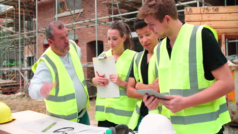 builder on building site discussing work with apprentices