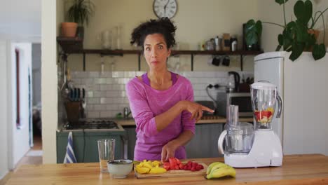 Portrait-of-mixed-race-female-vlogger-making-fruit-juice-in-the-kitchen-at-home