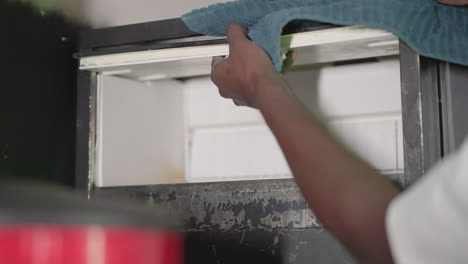 Close-up of person in white shirt reaching up to place a cloth in a storage space. Focus on hand and cloth with a blurred background, conveying a sense of calm action and precision in a tidy environment
