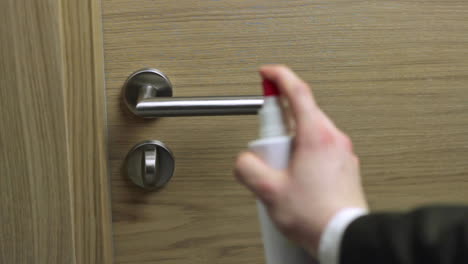 spraying a metallic door handle with a disinfectant cleanser to sterilise it to avoid spreading germs