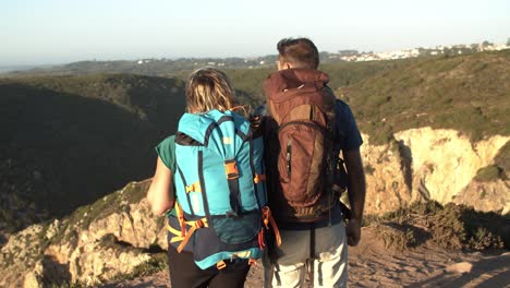 couple with camping backpacks standing at cliff