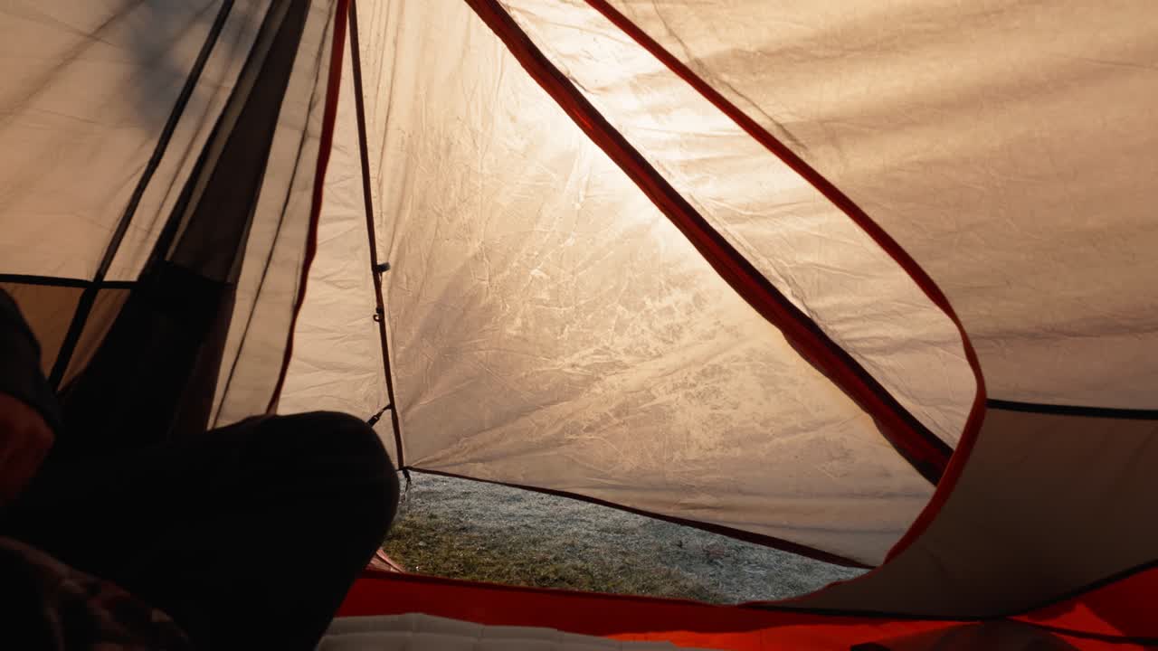 Shot from inside a camping tent showing a hiker unzipping and re-zipping the tent flap to check the sunrise view outside.