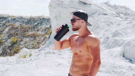 strong shirtless athlete drinks water from a bottle. training in sports in nature