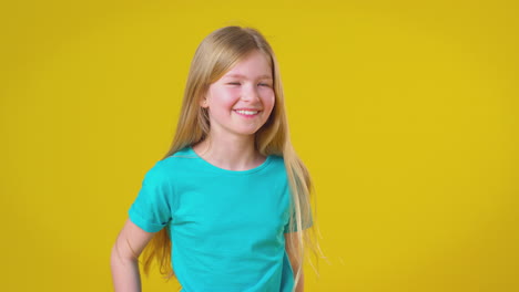 studio portrait of girl with long hair laughing against yellow background