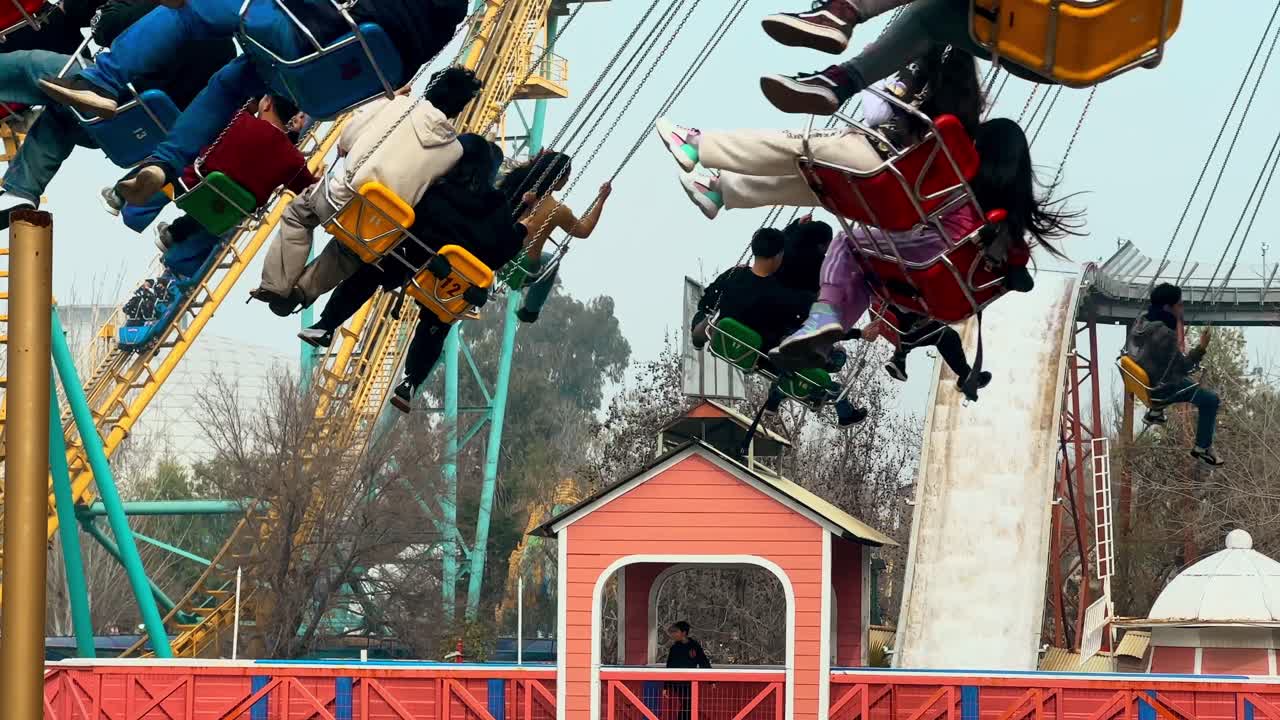 Spinning chairs passing by full of people establishing in the amusement park in Fantasilandia, tsunami attraction in the background. Family atmosphere