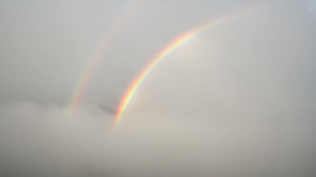 A Stunning Double Rainbow Emerges from Behind Soft, Gray Clouds, Creating a Breathtaking Arc of Colors Against the Mellow Sky