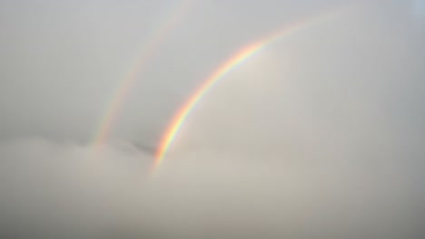 a stunning double rainbow emerges from behind soft, gray clouds, creating a breathtaking arc of colors against the mellow sky